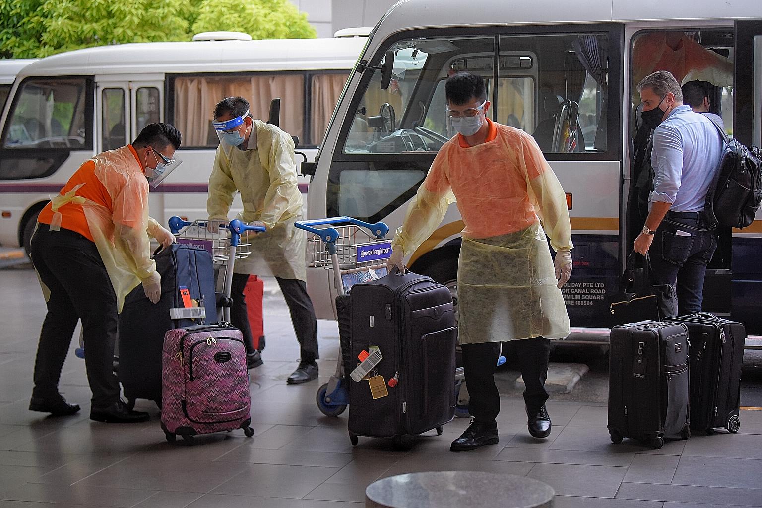 Attendants at Changi Airport's Terminal 3 handling luggage belonging to passengers from a flight which arrived from London yesterday, as the passengers boarded buses that would take them to dedicated facilities to serve their stay-home notice.