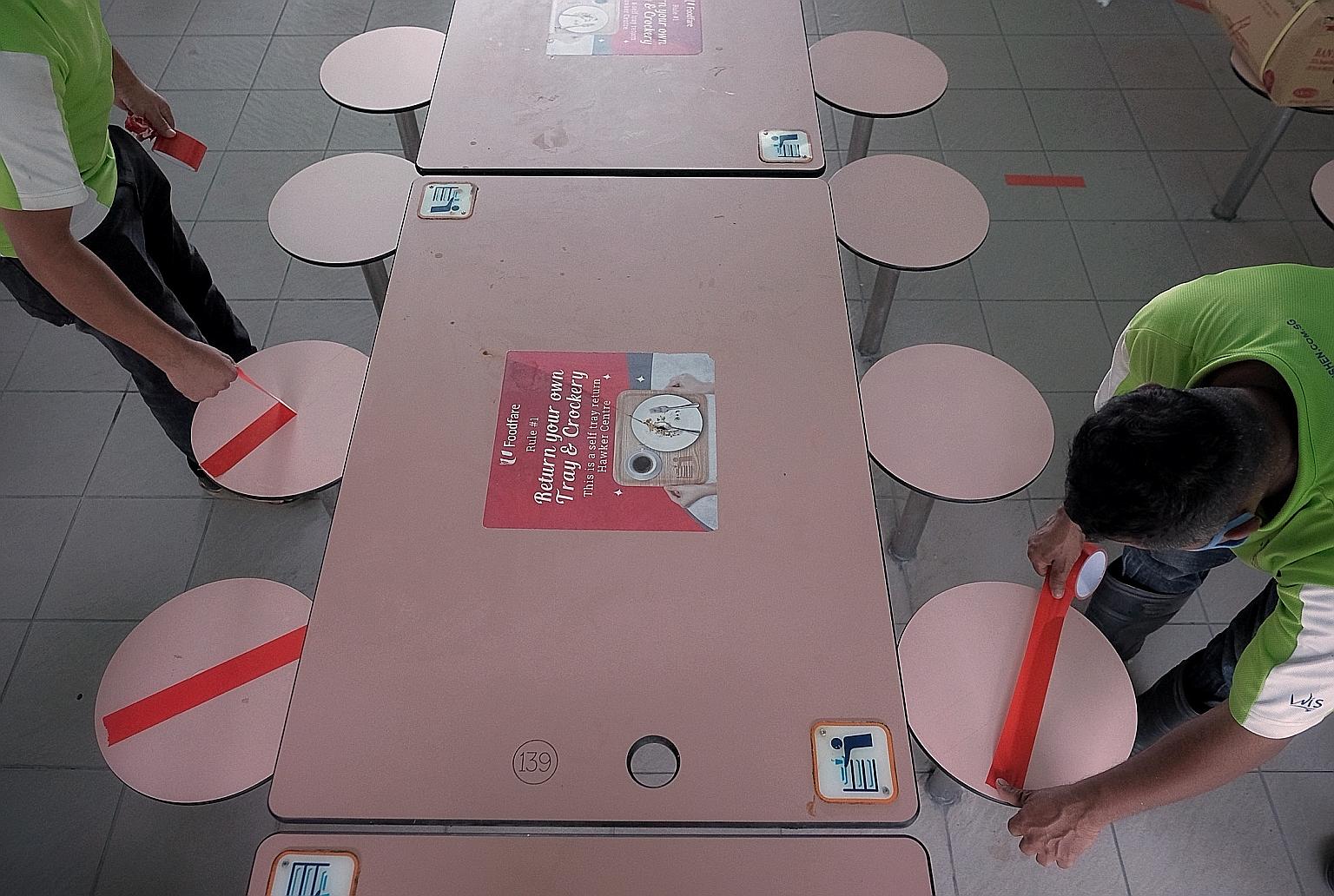 Workers adjusting safe distancing tape markings on seats at Whampoa Food Centre yesterday, in preparation for an increase in permitted dining group sizes to a maximum of eight people, from five people previously, as Singapore moves into the third pha