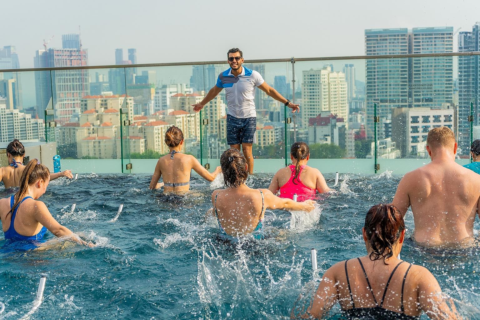 Participants pedalling on stationary bikes in a pool during an Aquaspin class led by co-founder Yannick Dedigama at Hotel Jen Orchardgateway.