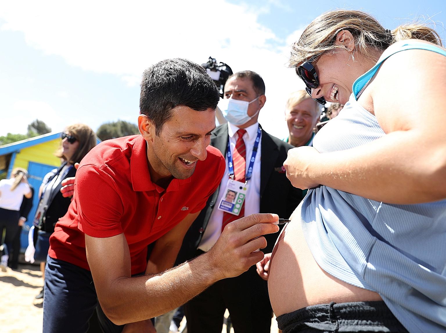 Novak Djokovic signing an expectant mother's belly while parading his Australian Open trophy at Melbourne's Brighton Beach.