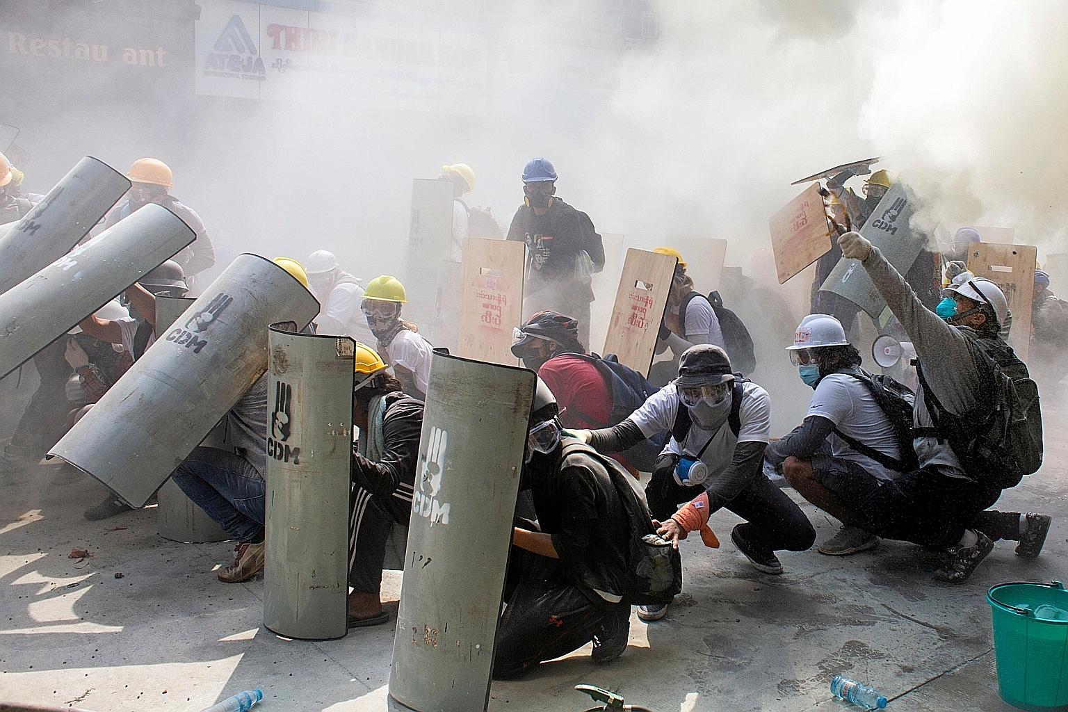 Protesters taking cover during a clash with riot police officers in Yangon yesterday. Myanmar police and soldiers moved quickly yesterday to stamp out protests across the nation, firing live bullets at demonstrators in Yangon and other cities when st