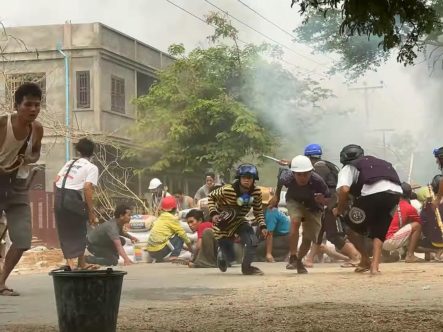 Protesters taking cover during clashes with security forces in Monywa, Myanmar, yesterday. One man was killed and several were wounded when police opened fire on a group in the town.
