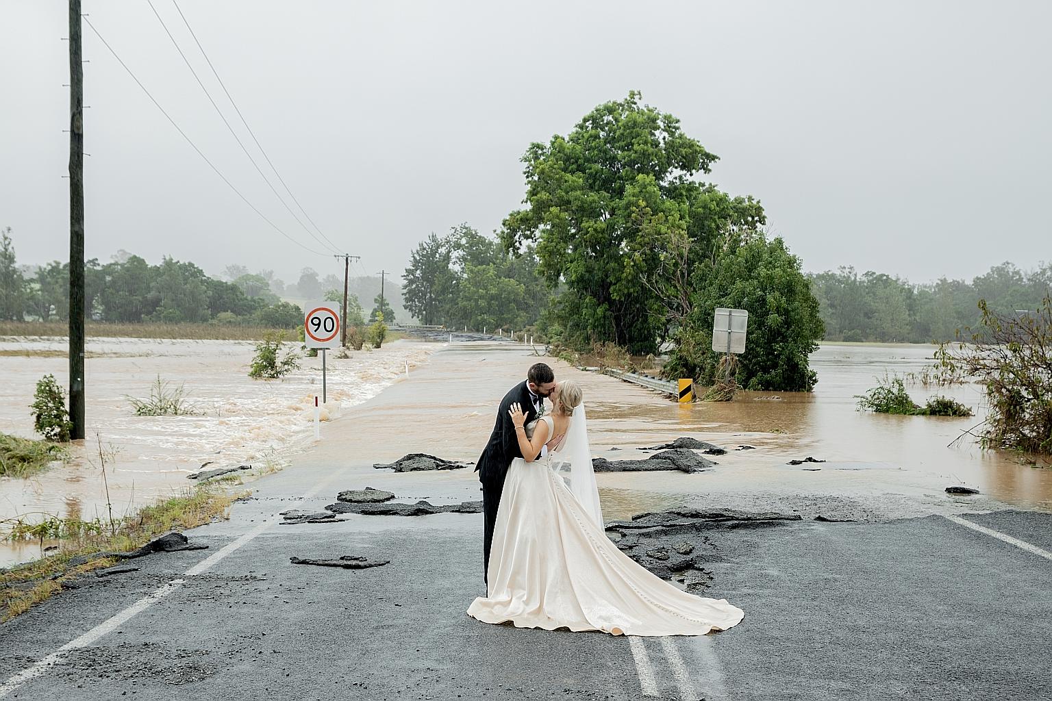 Newlyweds Kate Fotheringham and Wayne Bell in Wingham, New South Wales. Behind them is a bridge submerged in floodwaters, which made it impossible for the bride and her family to drive from their home to Wingham for the wedding on Saturday. Instead,