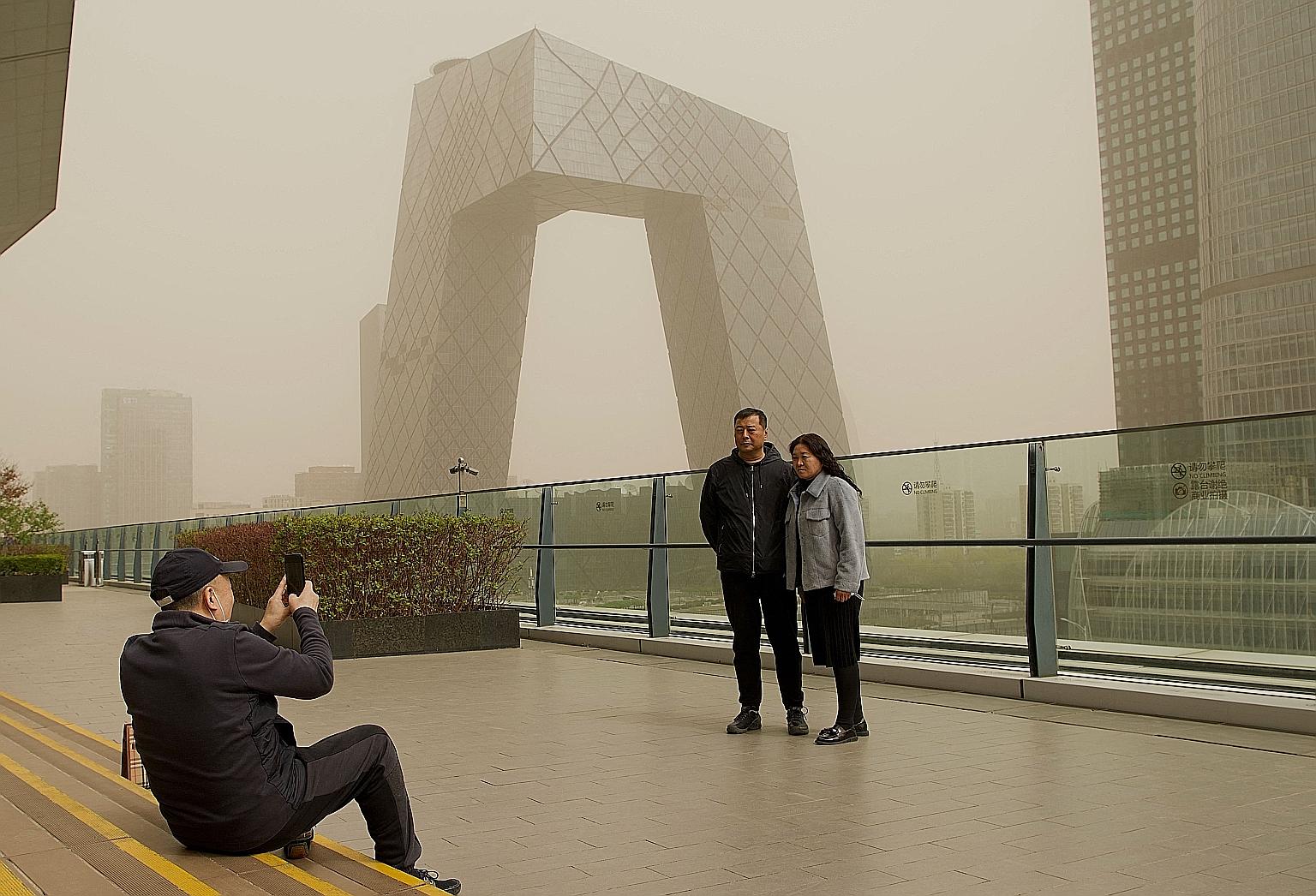 People posing for a picture before the China Central Television headquarters during a sandstorm in Beijing yesterday. The sandstorm caused the sky to turn yellow and reduced visibility to less than 1,000m.