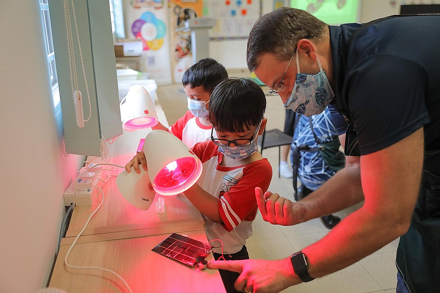 Primary 2 pupils from Big Heart Student Care Centre at Teck Whye Primary School shining a light on a solar panel that powers a small motor at the first workshop yesterday under the 3M Tinkering Headstart at South West Programme - a collaboration bet