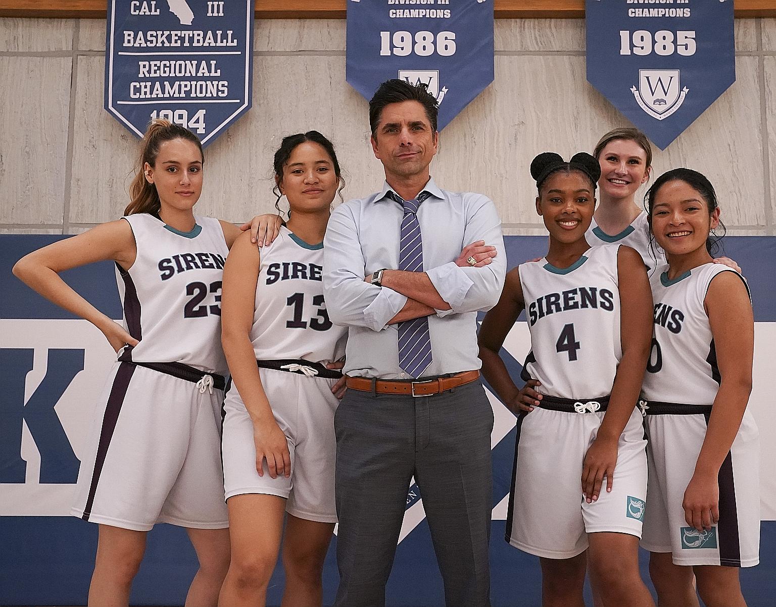 John Stamos as coach Marvyn Korn with the girls' high school basketball team members played by (from far left) Nell Verlaque, Tiana Le, Monique Green, Cricket Wampler and Tisha Custodio.