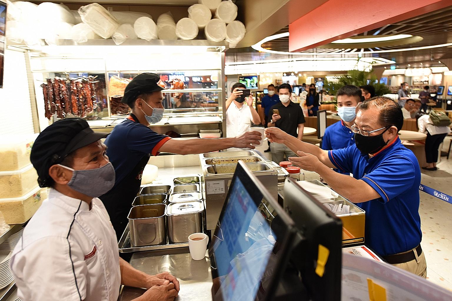 Mr Seah Kian Peng, group chief executive officer of NTUC Enterprise and FairPrice Group, serving coffee to chef Chan Hon Meng and another staff member of Hawker Chan during a meet-and-greet session at the newly renovated Kopitiam foodcourt in Plaza S