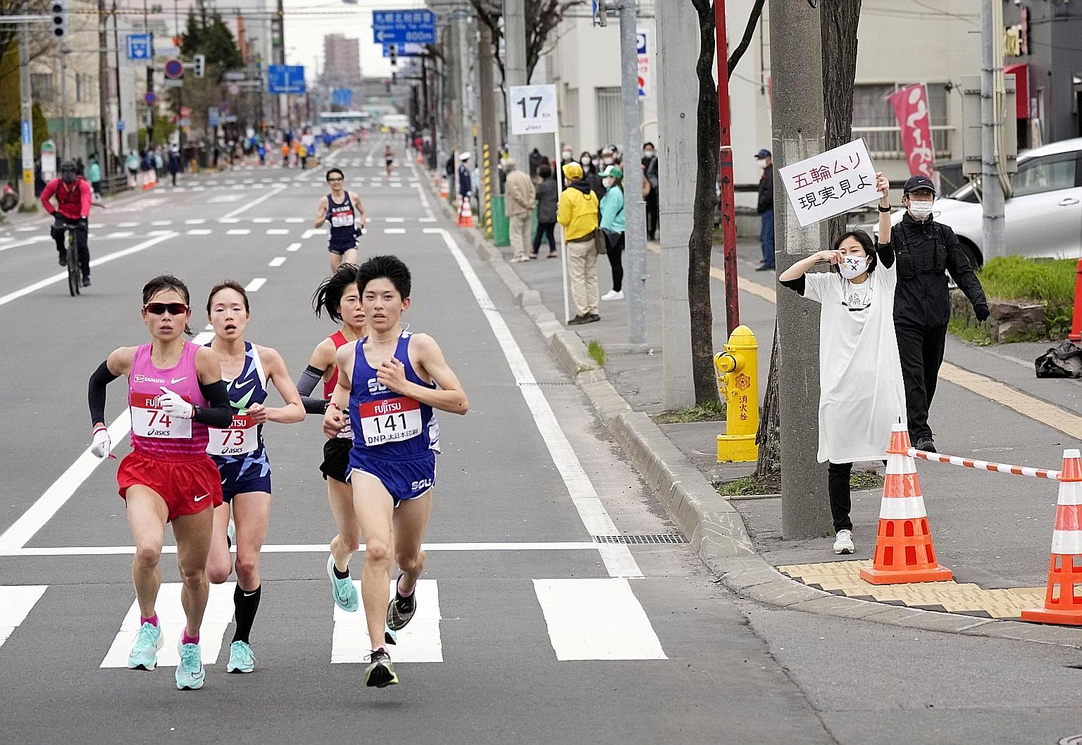A spectator raising a sign reading "It is impossible to hold the Olympics, face up to reality" during a half-marathon in Sapporo on May 5.
