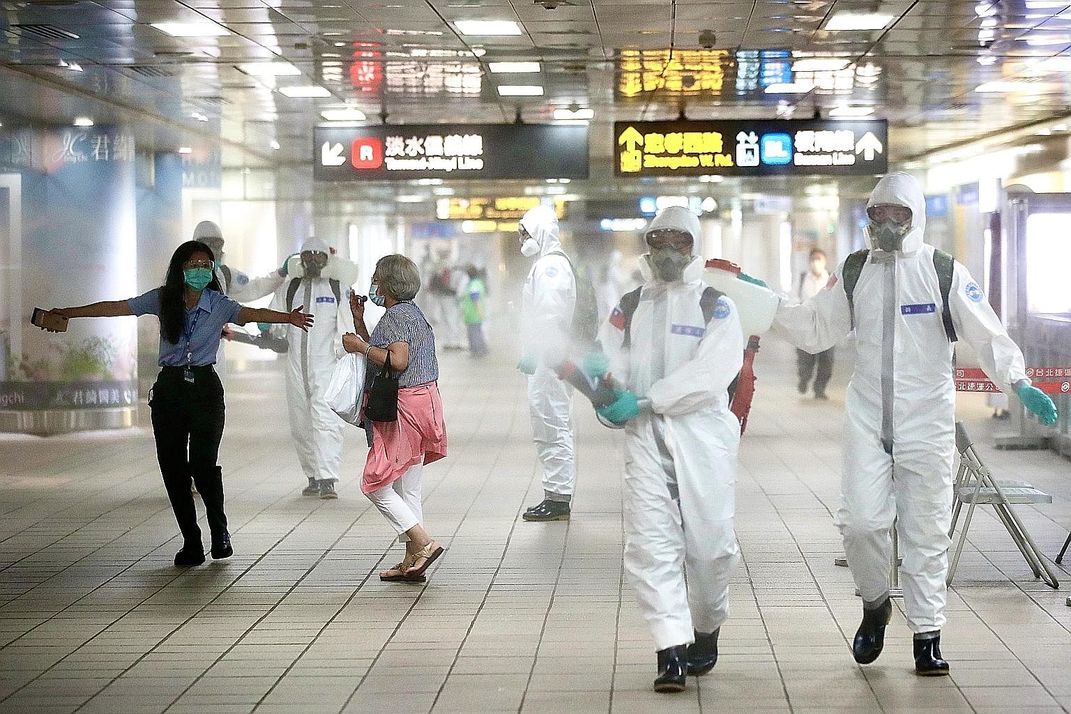 A passenger being ushered away from military personnel spraying disinfectant yesterday at Taipei Main Station in Taiwan. The island said yesterday that all schools would close until the end of next week, with classes shifted online amid a spike in Co