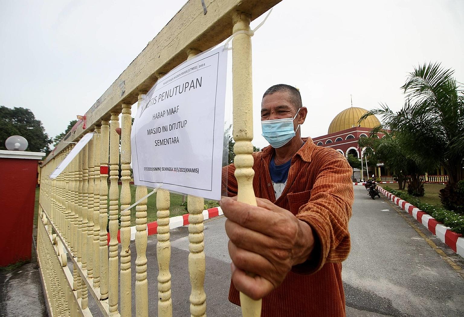 A man putting up a notice of temporary closure of the Raja Nazrin Shah Mosque in Kampung Rapat Jaya Tambahan, Ipoh, yesterday. Malaysia's vaccination roll-out is moving at a slower pace than initially scheduled due to the slow arrival of vaccines. PH