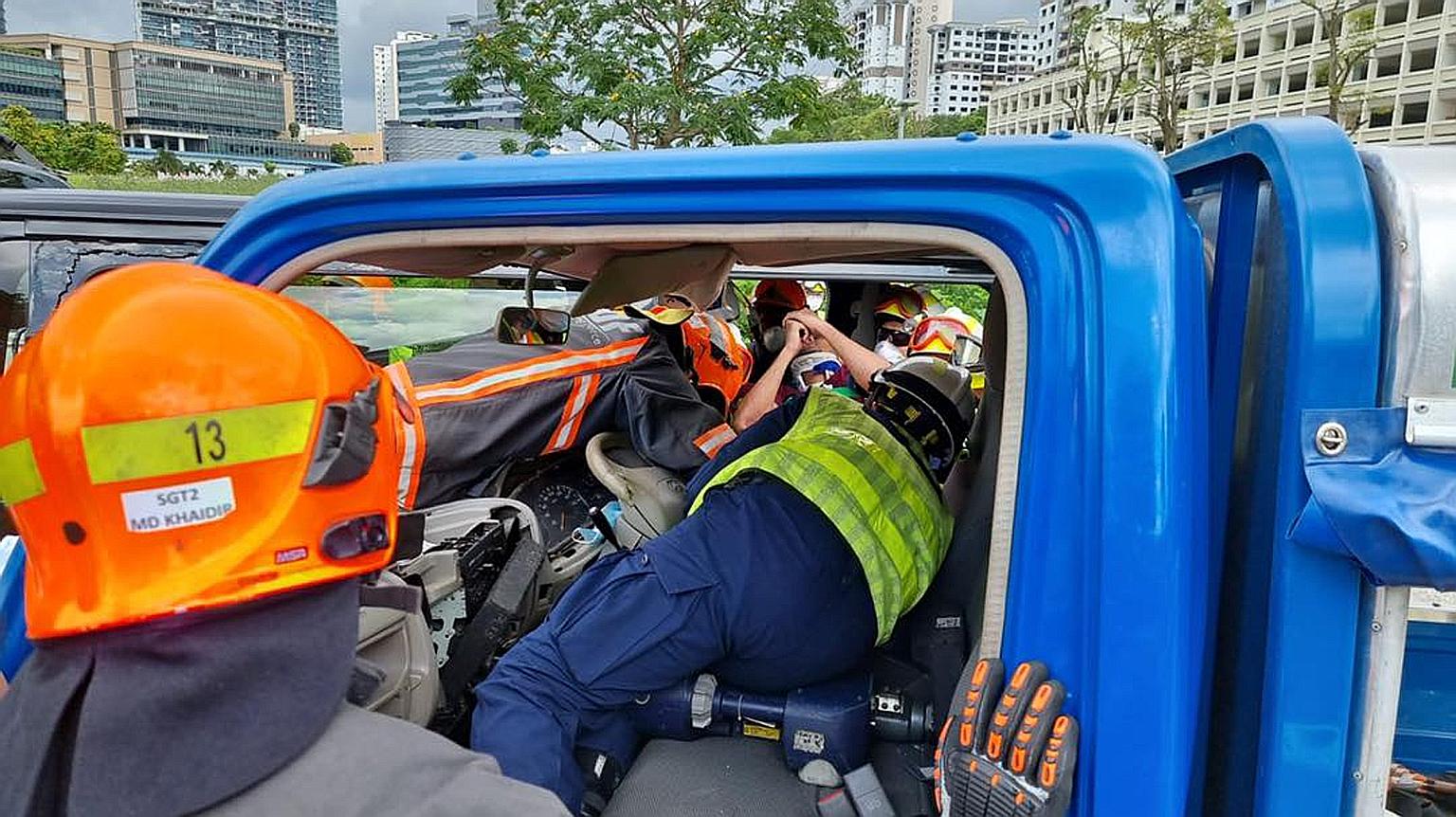 Singapore Civil Defence Force rescuers (far left) working to free the lorry driver who was left trapped in his seat after an accident with a van (left) near the junction of Toh Guan Road and Toh Guan Road East yesterday. The lorry's cabin was crushed