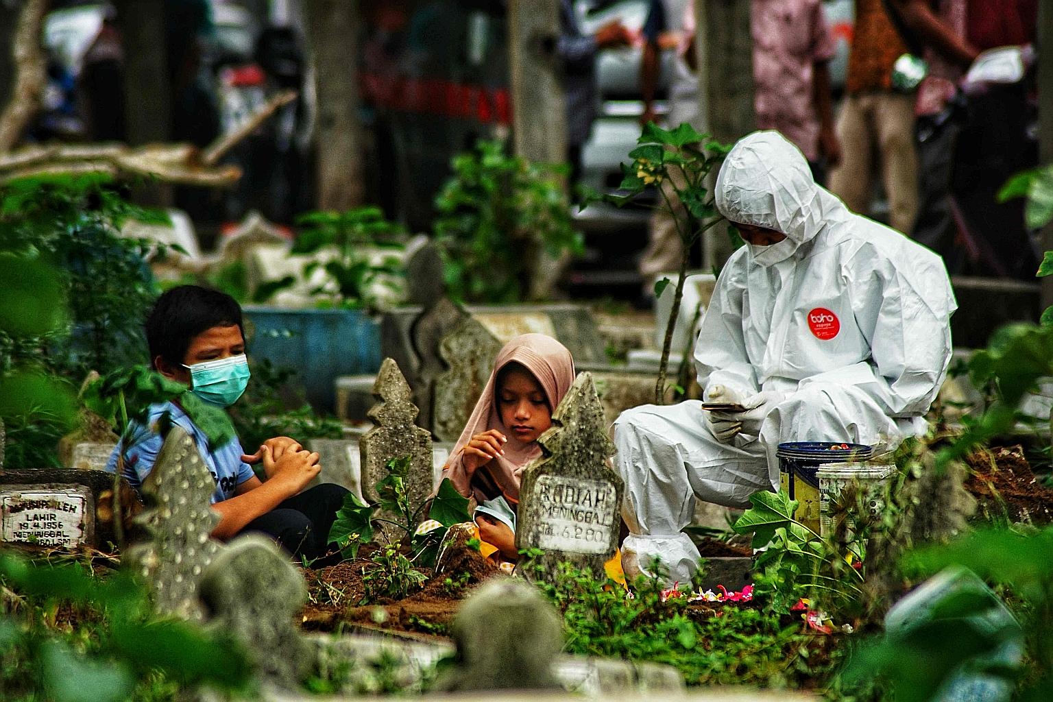 Two children and a family member wearing personal protective equipment praying by the grave of a Covid-19 victim at a cemetery in Lhokseumawe, Aceh, on Tuesday. The Independent Panel for Pandemic Preparedness and Response found gaps and failings at e