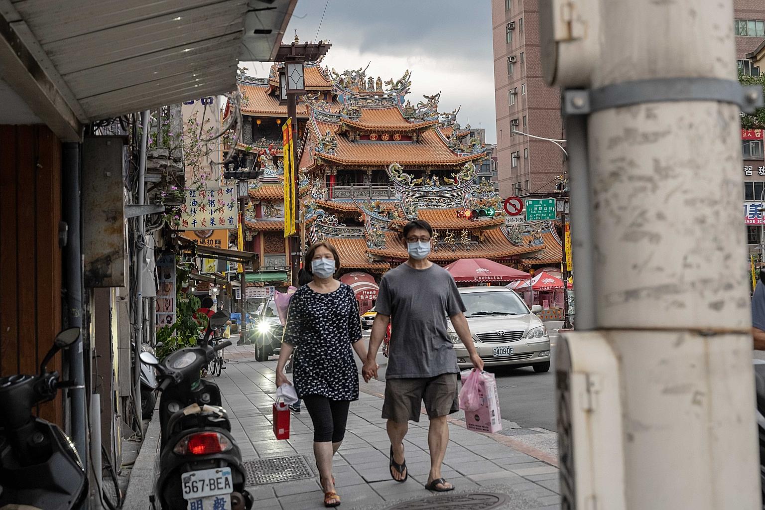 Pedestrians wear protective masks while walking through a market in Taipei on Friday. Since Wednesday, the island has been under Level 3 which requires people to wear masks once they leave their residences and prohibits any gathering of over five peo