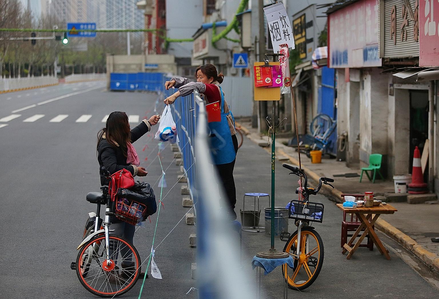 A woman delivering food to a resident over a barrier set up to prevent people from entering or leaving a residential community in Wuhan, in March last year. Muscular measures - a combination of centralised policy and grassroots mobilisation - have be