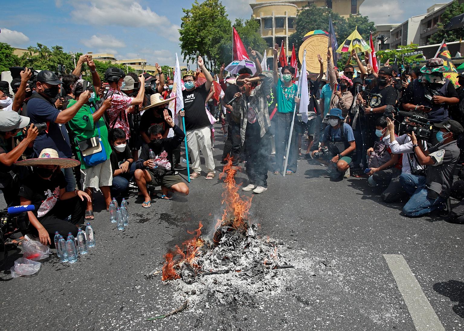 Protest leader Parit Chiwarak (centre) and other demonstrators setting fire yesterday to a Democracy Monument model, to mark the 89th anniversary of the abolition of absolute monarchy in Bangkok.