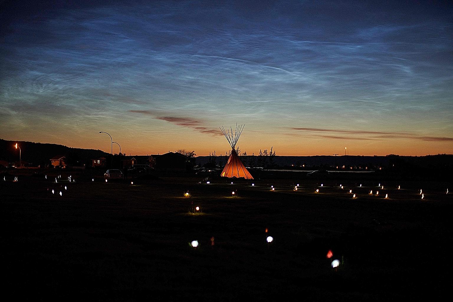 Above: Flames engulf a church in Morinville on Wednesday. The fires at this church and another near Halifax were being probed as possible arson. PHOTO: REUTERS Left: Solar lights and flags mark the spots at a former residential school in Saskatchewan