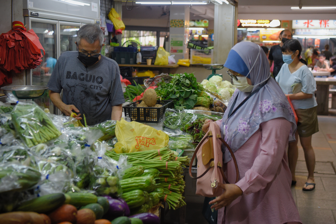 People purchase vegetables at 42-year-old Mr Mic Ng’s vegetable stall at Clementi 448 Market on 22 December, 2021. According to him, prices of some vegetables including tomatoes, long beans and eggplants have increased as a knock on efffect from the flo