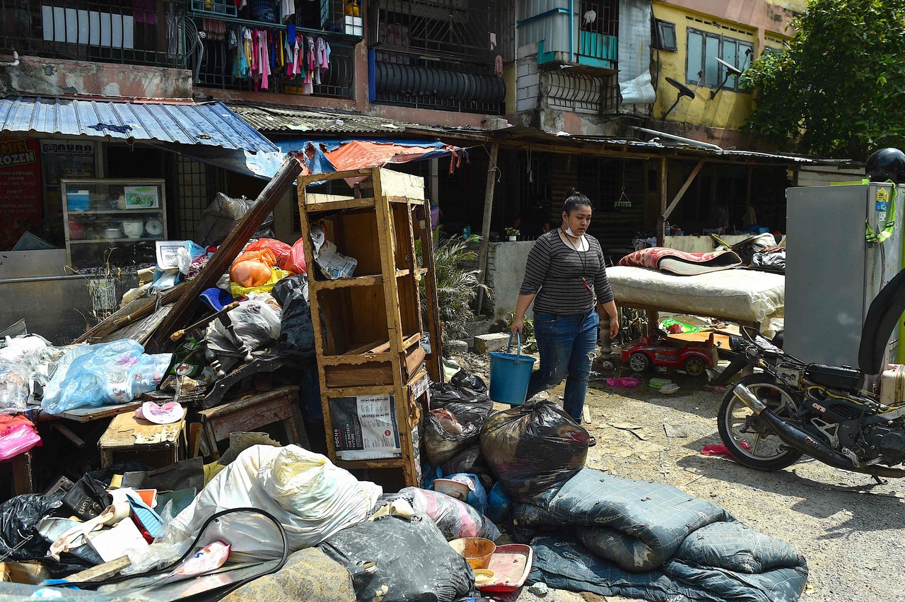 <p>A woman walks past items from her household, which were damaged during the recent floods, in Shah Alam, Selangor on December 27, 2021. (Photo by Arif KARTONO / AFP)</p>