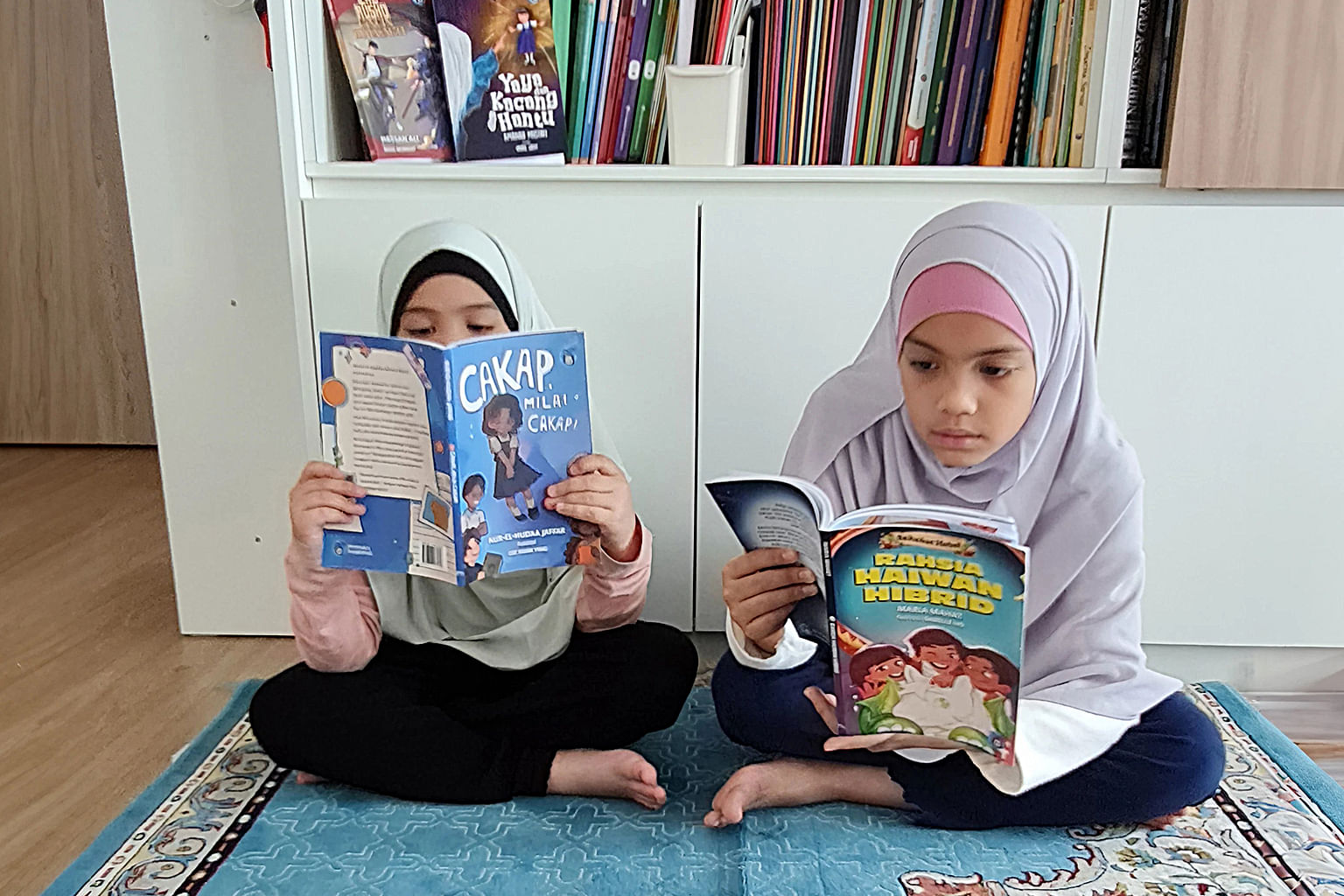 two muslim girls reading malay children's books by singaporean authors