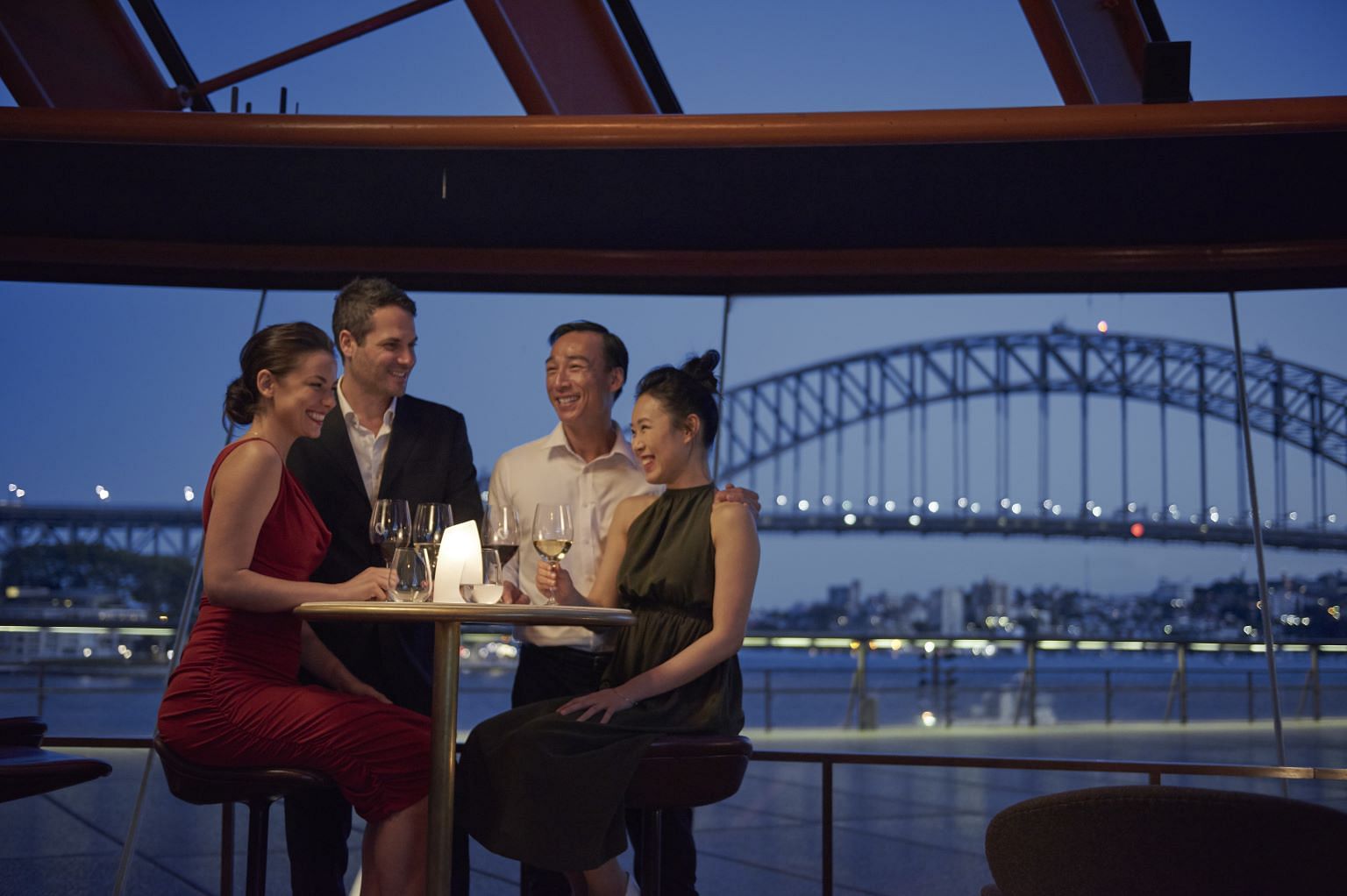 Couples sitting at Bennelong Restaurant enjoying dinner and drinks with the Sydney Harbour Bridge in the background