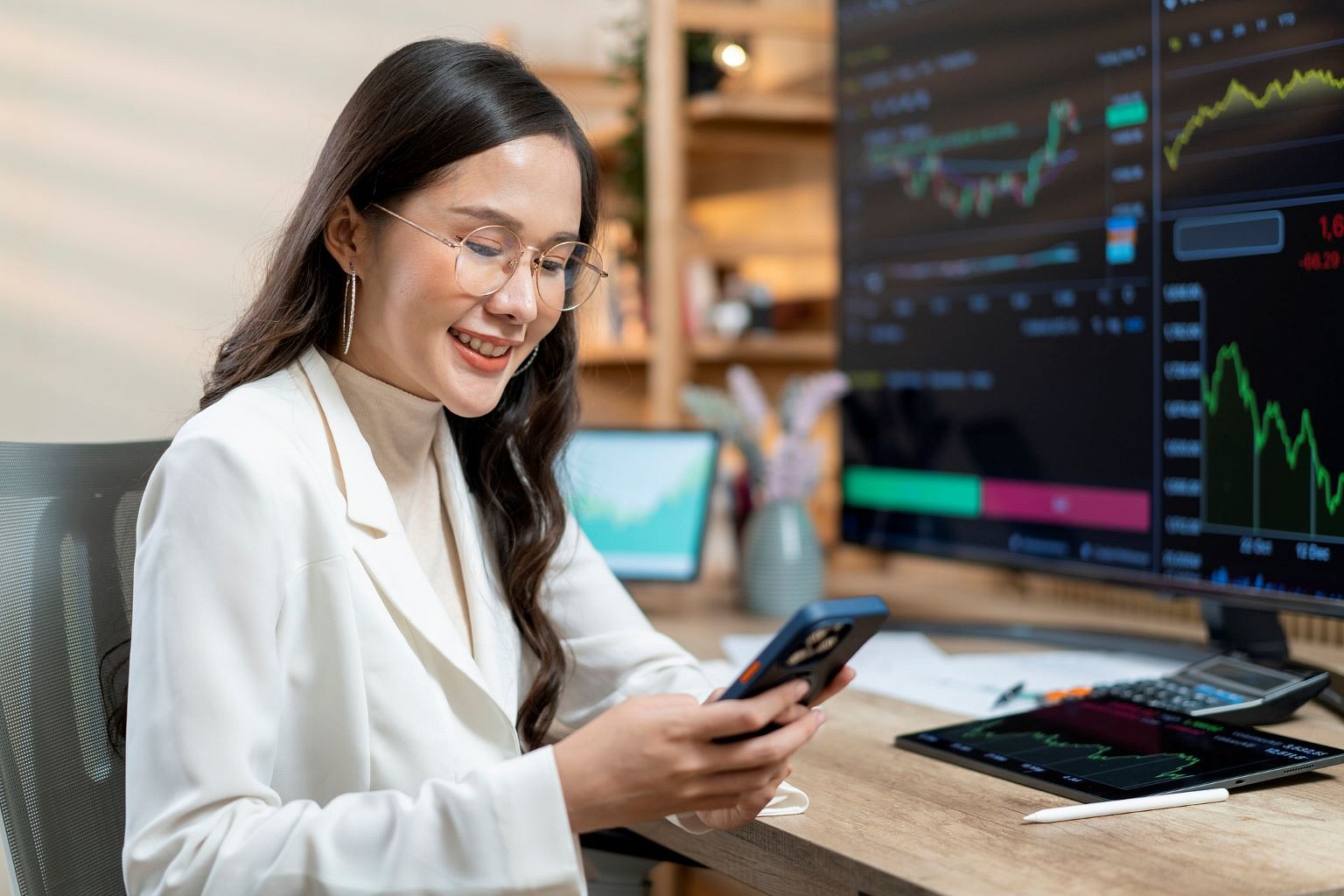 Woman sitting at her table looking at her phone and monitoring stocks