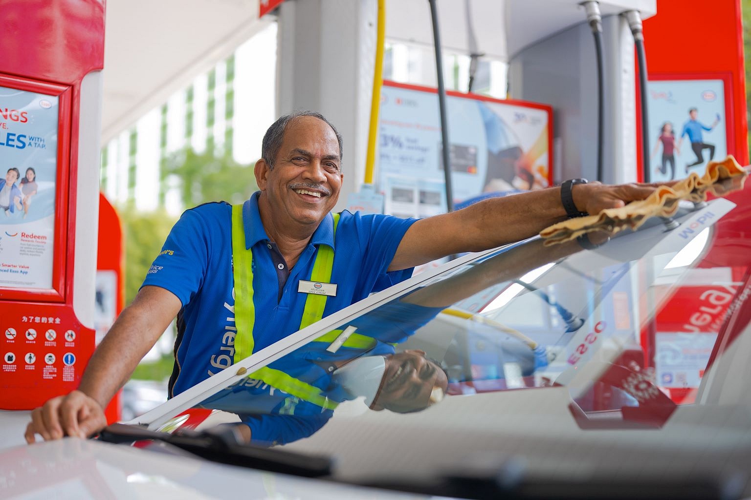 Indian male Esso pump attendant wiping a car and smiling