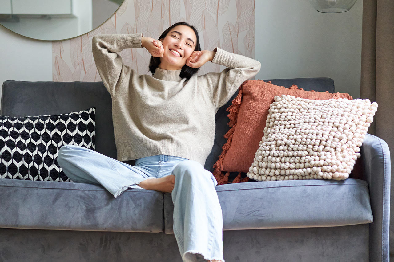 Asian woman sitting on a couch with both hands up feeling happy and well
