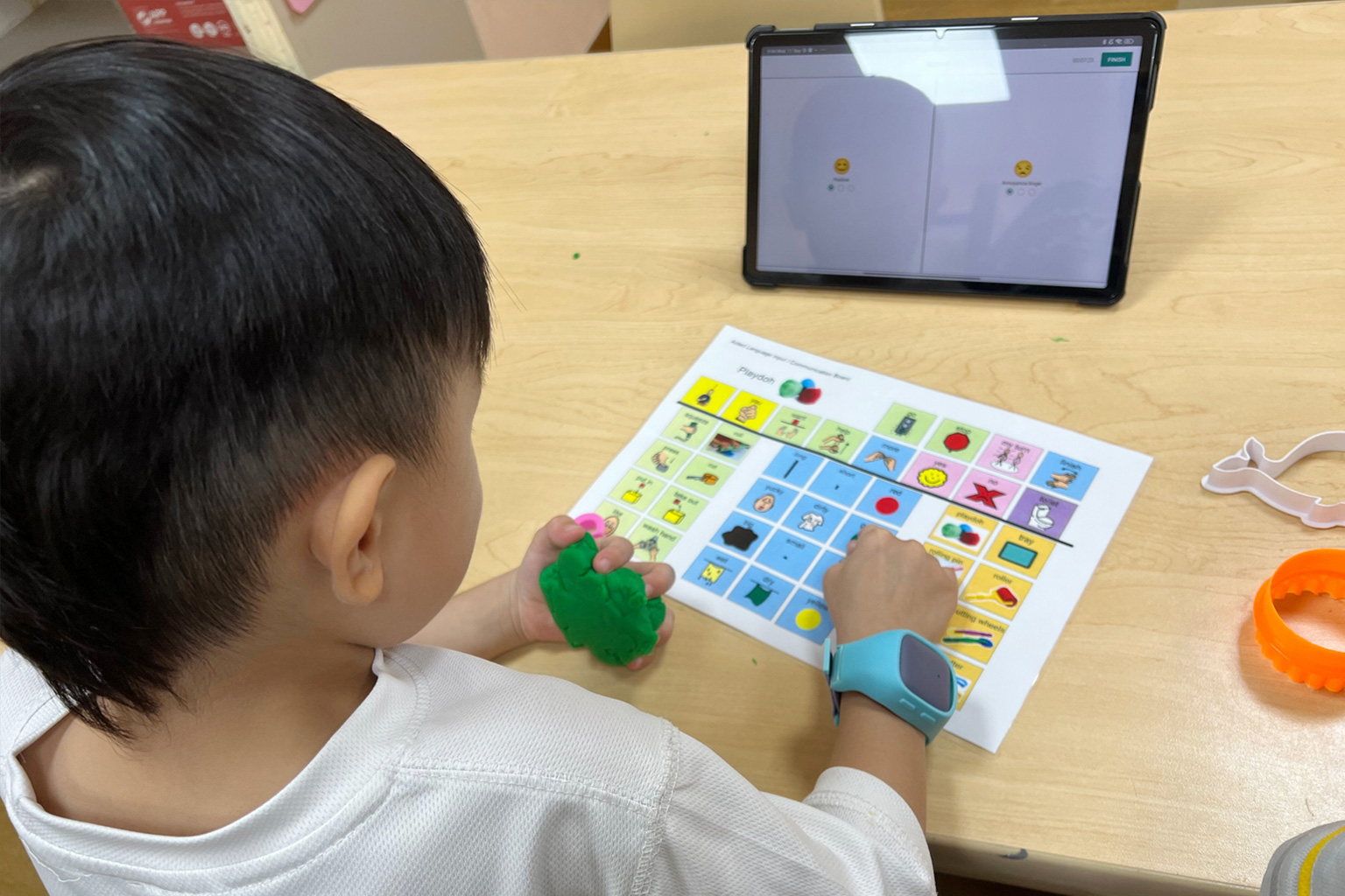 A student at Thye Hua Kwan Moral Charities Early Intervention Programme for Infants and Children wearing the Pelios watch on his wrist, with his female teacher looking at a tablet