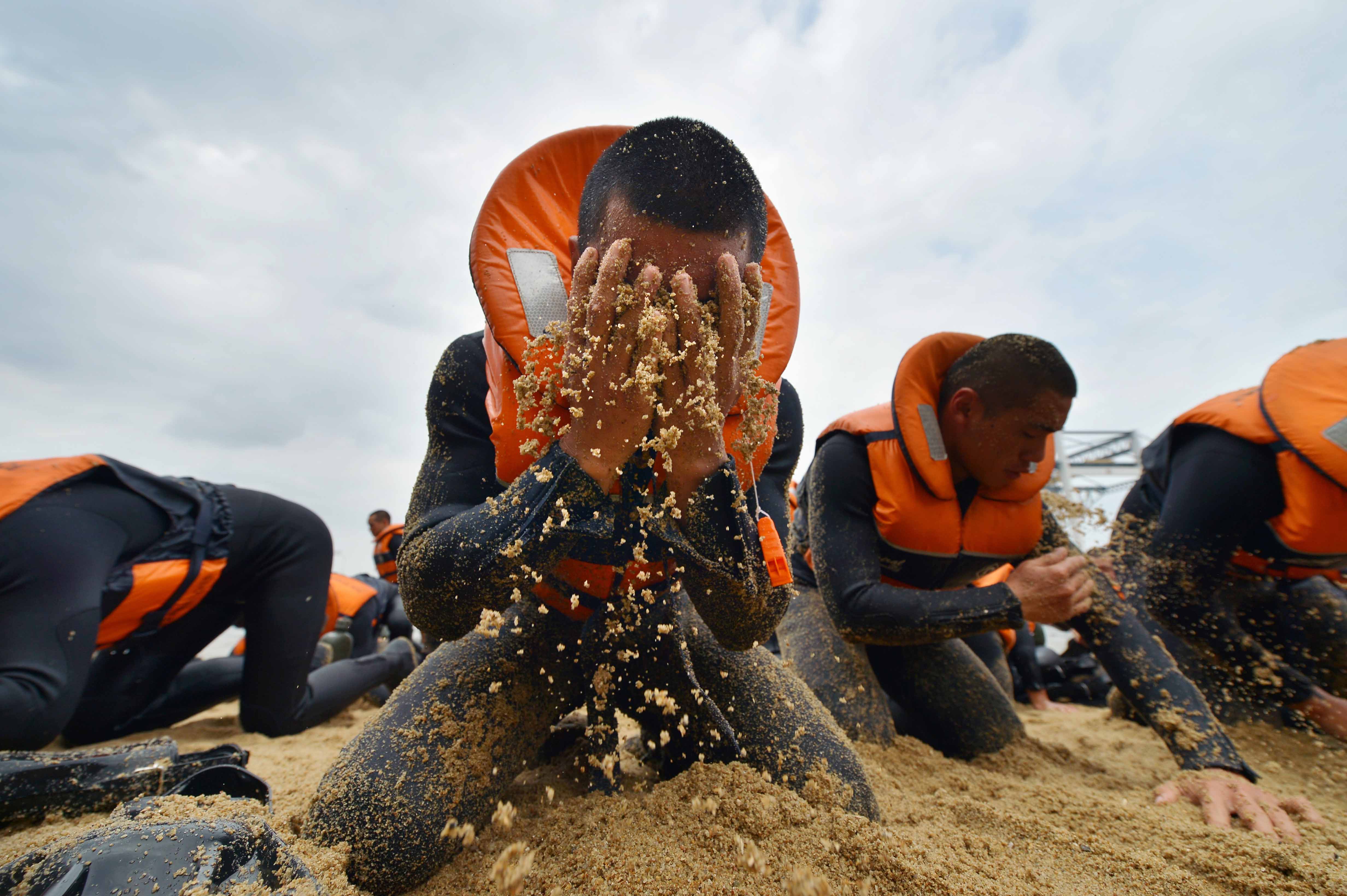Trainees (above) covering themselves with sand during an exercise in the five-month Combat Diver Course. It was an equally gritty task for ST photojournalist Alphonsus Chern (left), seen here hauling himself up a rope at the Sembawang Camp jetty.