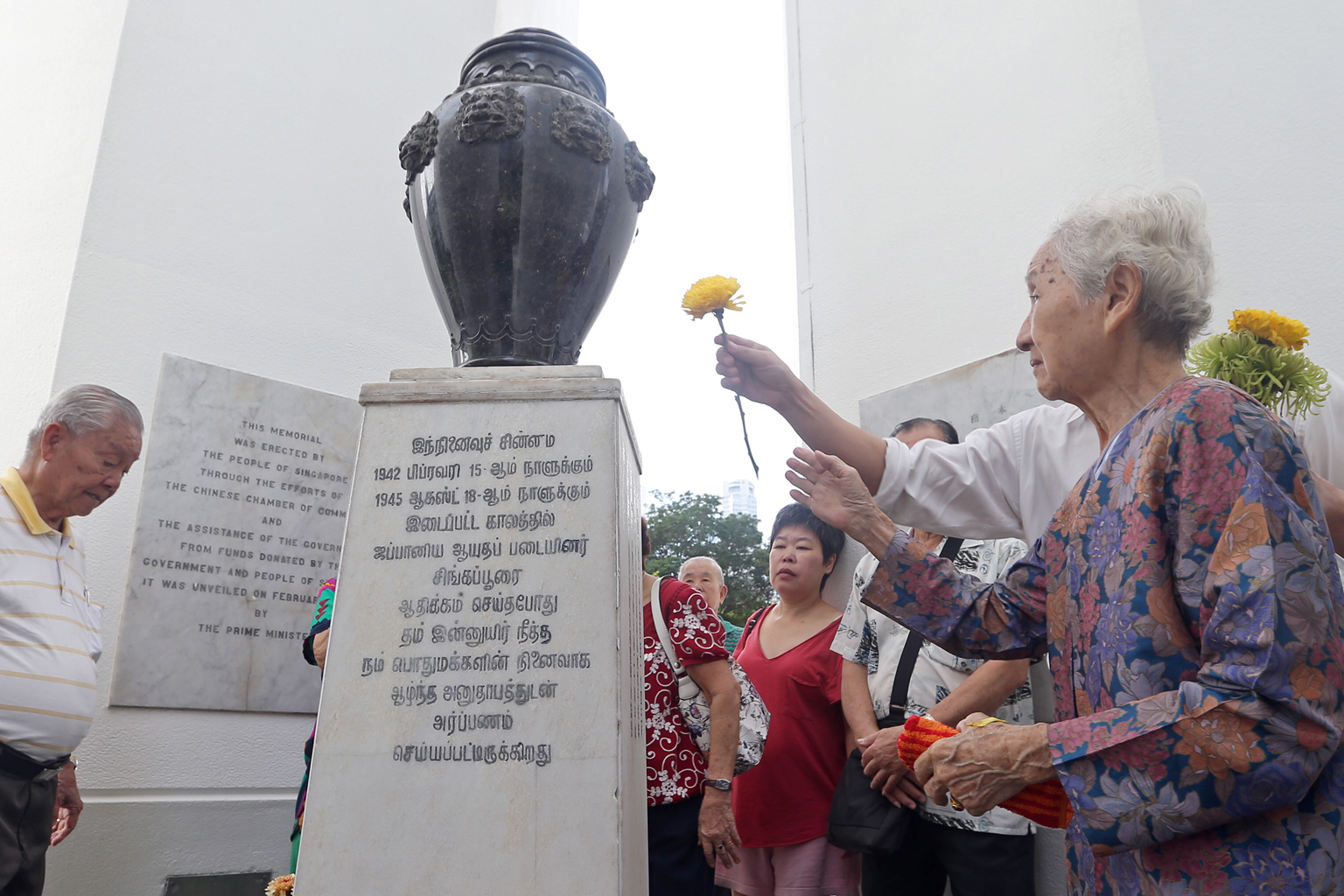 Madam Lim Geok Hong (right), 83, and her son John Teo (partially hidden, laying a flower), 50, at the Civilian War Memorial along with other participants of the 49th War Memorial Service yesterday.