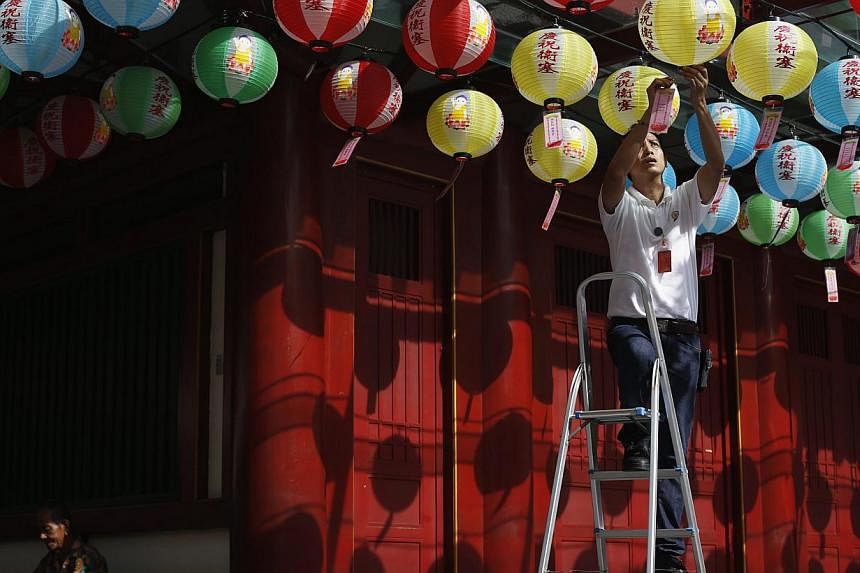 A temple worker hangs well wishes written by donors to lanterns outside the Buddha Tooth Relic Temple ahead of Vesak Day in Singapore on May 6, 2014. -- FILE PHOTO: REUTERS