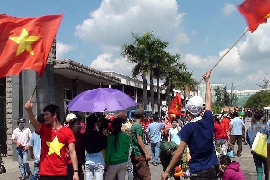 A photo made available May 14, 2014 shows workers waving Vietnamese flags outside a factory in the Binh Duong province, Vietnam, on May 13, 2014. -- FILE PHOTO: EPA