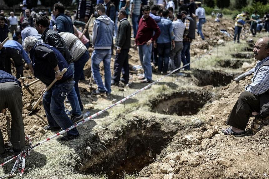 People gather around empty graves during a funeral ceremony of miners who died in an explosion on May 15, 2014, in the western town of Soma in the Manisa province. -- PHOTO : AFP