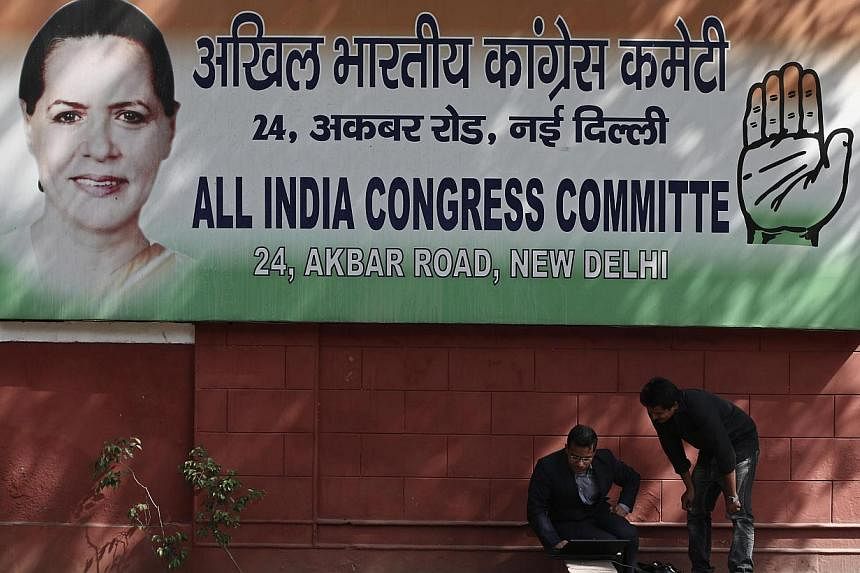 Men sit under a banner carrying a portrait of chief of India's Congress party Sonia Gandhi outside the Congress office in New Delhi May 16, 2014. -- PHOTO: REUTERS