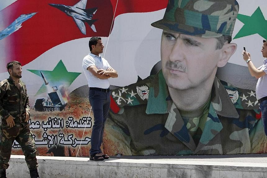 A man takes a photo of his friend in front of a poster of Syria's President Bashar al-Assad at Umayyad Square in Damascus on May 16, 2014. The UN Security Council is expected to vote Thursday on a resolution to haul Syria before the International Cri