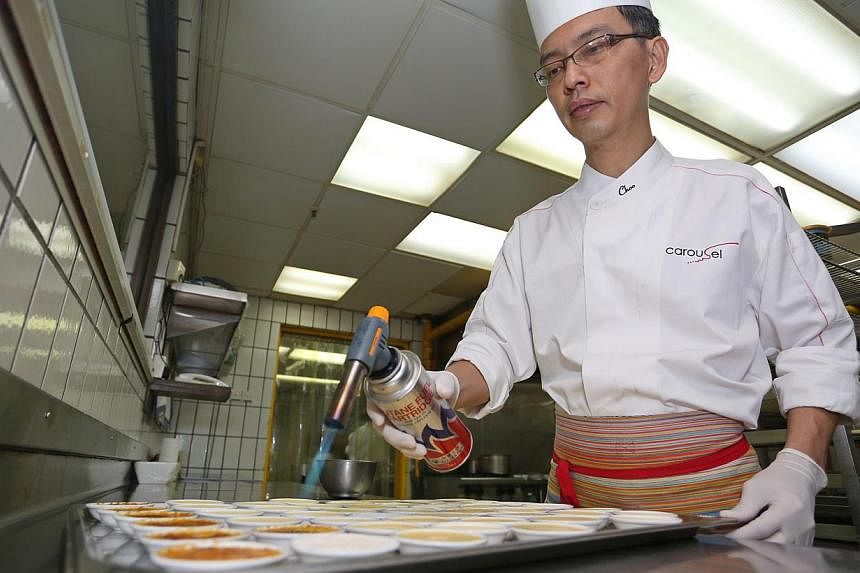 Executive pastry chef Choo Eng Tat from Royal Plaza on Scotts preparing creme brulee. At far left is the safety wall towards which blowtorches are to be pointed at all times. -- PHOTO: EDWARD TEO FOR THE SUNDAY TIMES