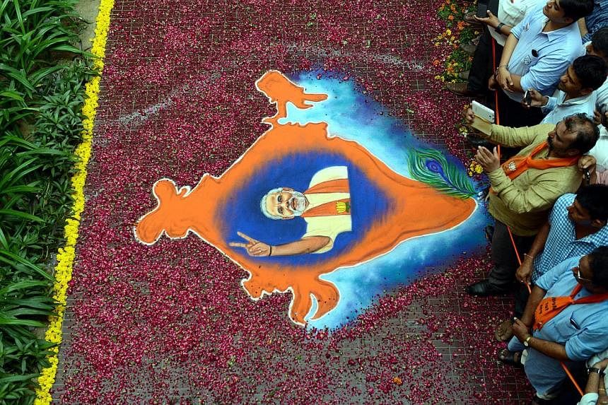 In this photograph taken on May 16, 2014, Indian supporters of the Bharatiya Janata Party (BJP) look on near a rangoli decoration bearing the image of BJP prime ministerial candidate Narendra Modi and the map of India at Shri Kamalam, the BJP Gujarat
