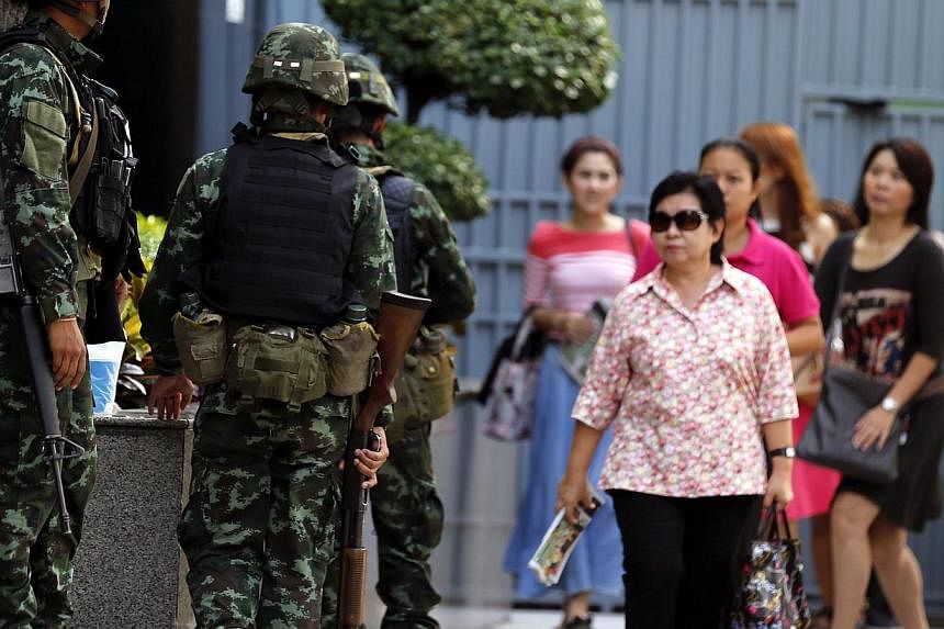 Thai office workers walk past armed soldiers standing guard outside the Shinawatra Tower Two in Bangkok, Thailand on May 20, 2014. -- PHOTO: EPA
