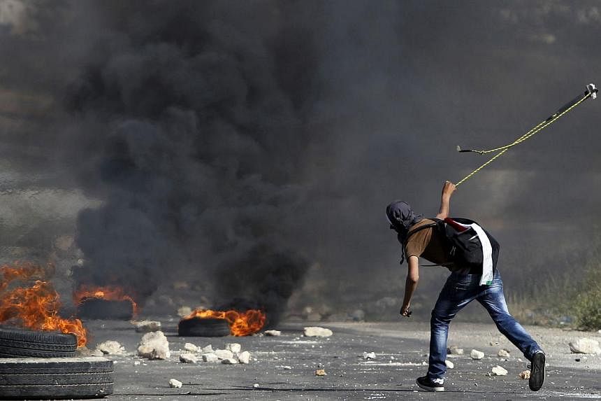 A masked Palestinian demonstrator uses a slingshot during clashes with members of the Israeli security forces outside the Israeli-run Ofer prison in the West Bank village of Betunia, on May 16, 2014, the day after two Palestinian youths were shot dea