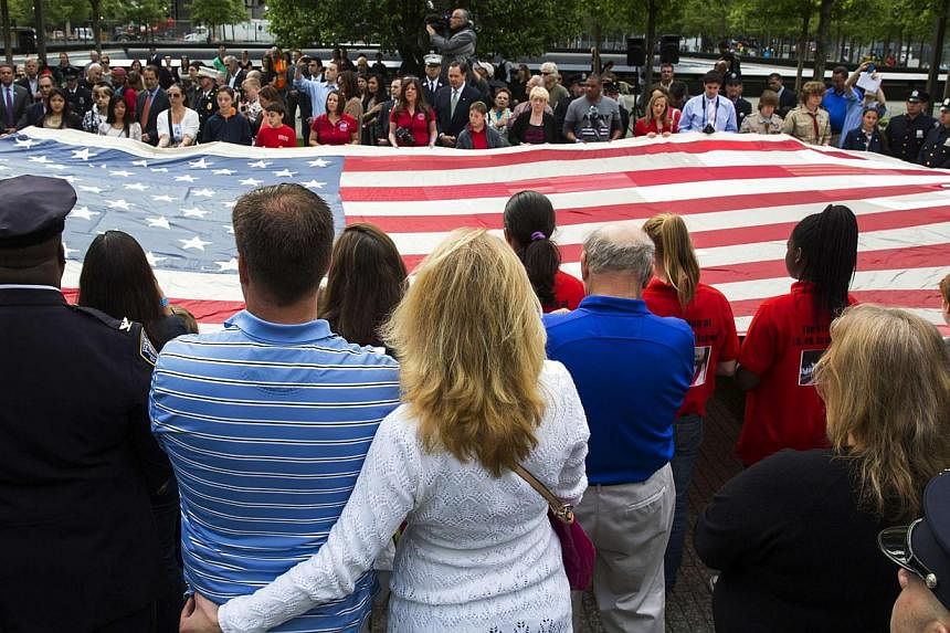 People designated to assist with transferring the National 9/11 Flag, donated by New York Says Thank You Foundation, hold it aloft on the grounds of the 9/11 Memorial Plaza before donating it to the National Sept 11 Memorial Museum in New York on May