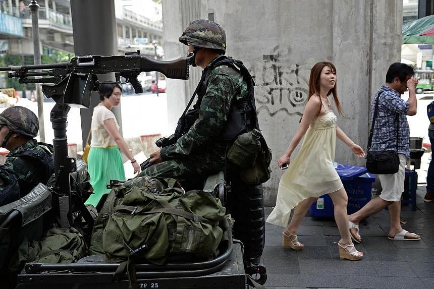 People walk past Thai army soldiers sitting in a jeep mounted with a machine gun as they secure a main intersection in Bangkok on May 20, 2014.&nbsp;The new ruling junta on Friday warned it would block any social media platforms in the country found 