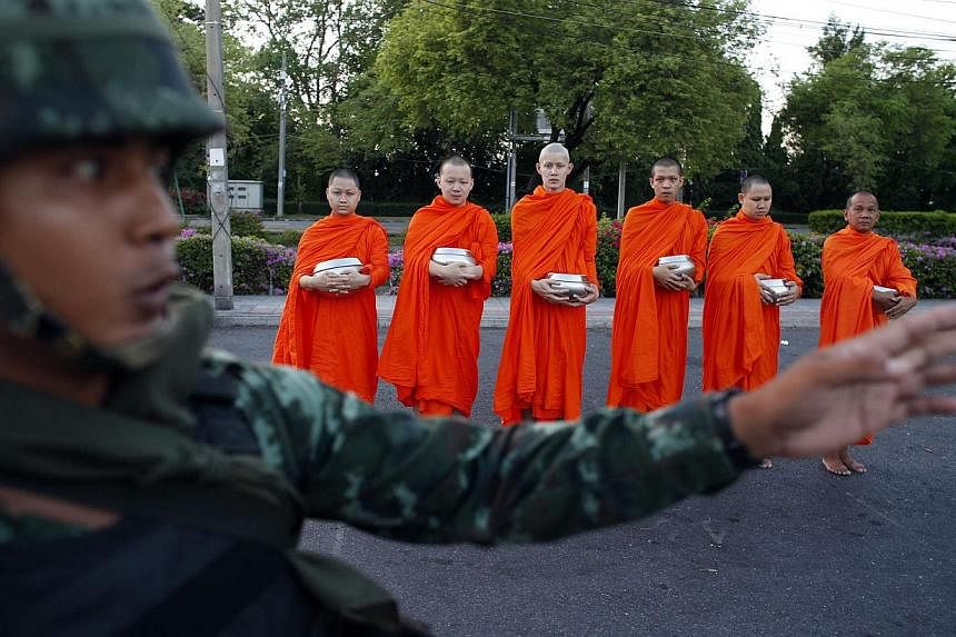 A Thai soldier stands guard while Buddhist monks beg for alms outside a temple near Government House in Bangkok on May 23, 2014. -- PHOTO: REUTERS