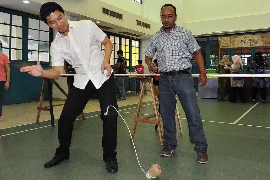 Minister for Manpower Tan Chuan-Jin tries out gasing, a traditional Malay game involving a spinning wooden top.&nbsp;-- PHOTO:&nbsp;DIOS VINCOY JR FOR THE STRAITS TIMES