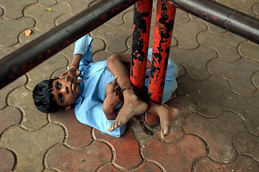 In this photograph taken on May 20, 2014 nine year old Indian boy Lakhan Kale is tied with a cloth rope around his ankle, to a bus-stop pole in Mumbai. Lakhan Kale cannot hear or speak and suffers from cerebral palsy and epilepsy, so his grandmother 