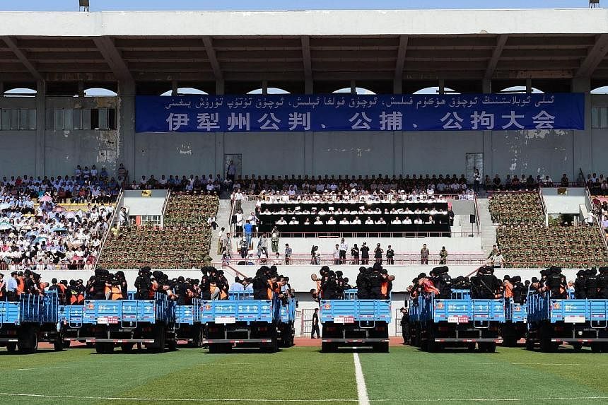This picture taken on May 27, 2014 shows security forces standing behing the accused wearing orange vests on trucks during a mass sentencing in Ili prefecture, northwest China's Xinjiang region. Authorities in China's mainly Muslim Xinjiang mounted a