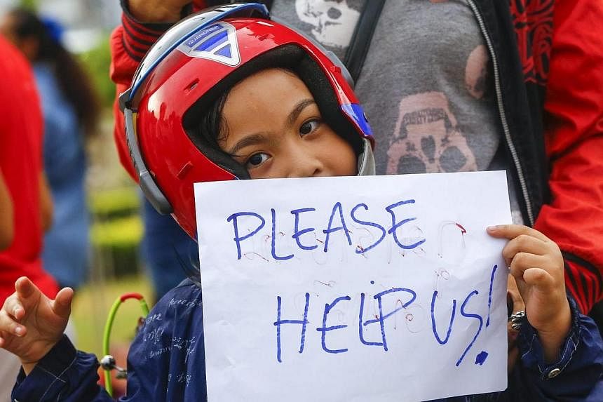 A young boy holds a sign reading 'Please help us', during a protest against the military coup at the victory monument in Bangkok, Thailand on May 27, 2014.&nbsp;A "closed for maintenance" sign hangs near Bangkok's historic Democracy Monument. -- PHOT