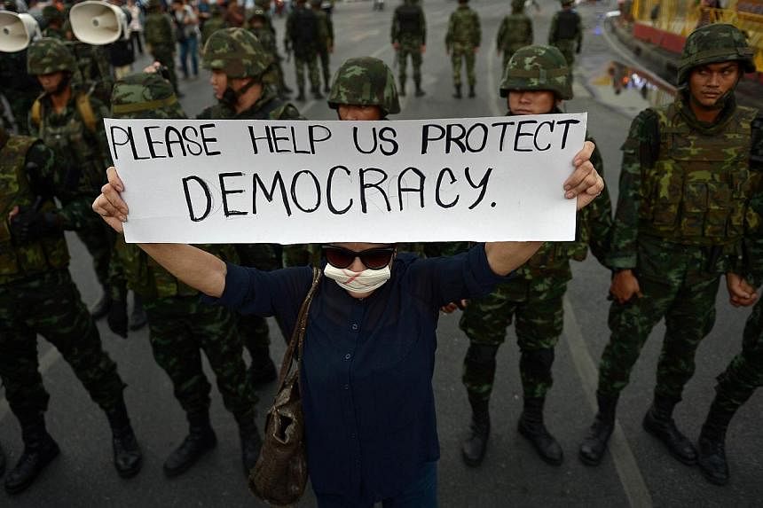 An anti-coup protester holds up a sign in front of soldiers as she takes part in a rally at Victory Monument in Bangkok on Monday. How the international society responds to coups varies greatly.