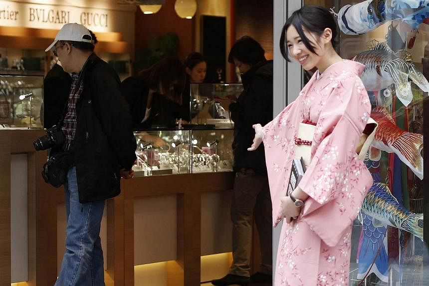 Tourists look at displays at a duty free store as a woman in Kimono welcomes visitors, along a street at Tokyo's Ginza Shopping district on May 15, 2014. Japan is no longer in a deflationary situation with consumer prices and corporate profits rising