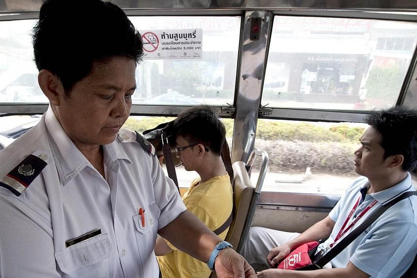 Thai bus fare collector Watcharee Viriya collects fares from passengers as the bus travels on a street in Bangkok.&nbsp;Stuck for hours each day in snarling traffic, bus conductors in Thailand's sprawling capital have found a radical solution to a la