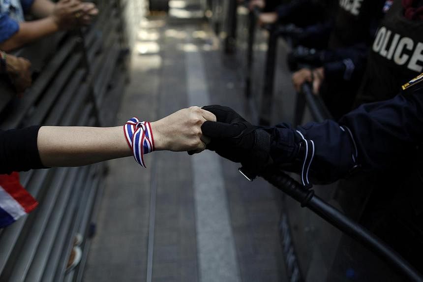 An anti-government protester holds hands with an anti-riot police officer across the closed gates outside the headquarters of the ruling Puea Thai Party of former prime minister Yingluck Shinawatra in Bangkok in this Nov 29, 2013, file photo.&nbsp;Th